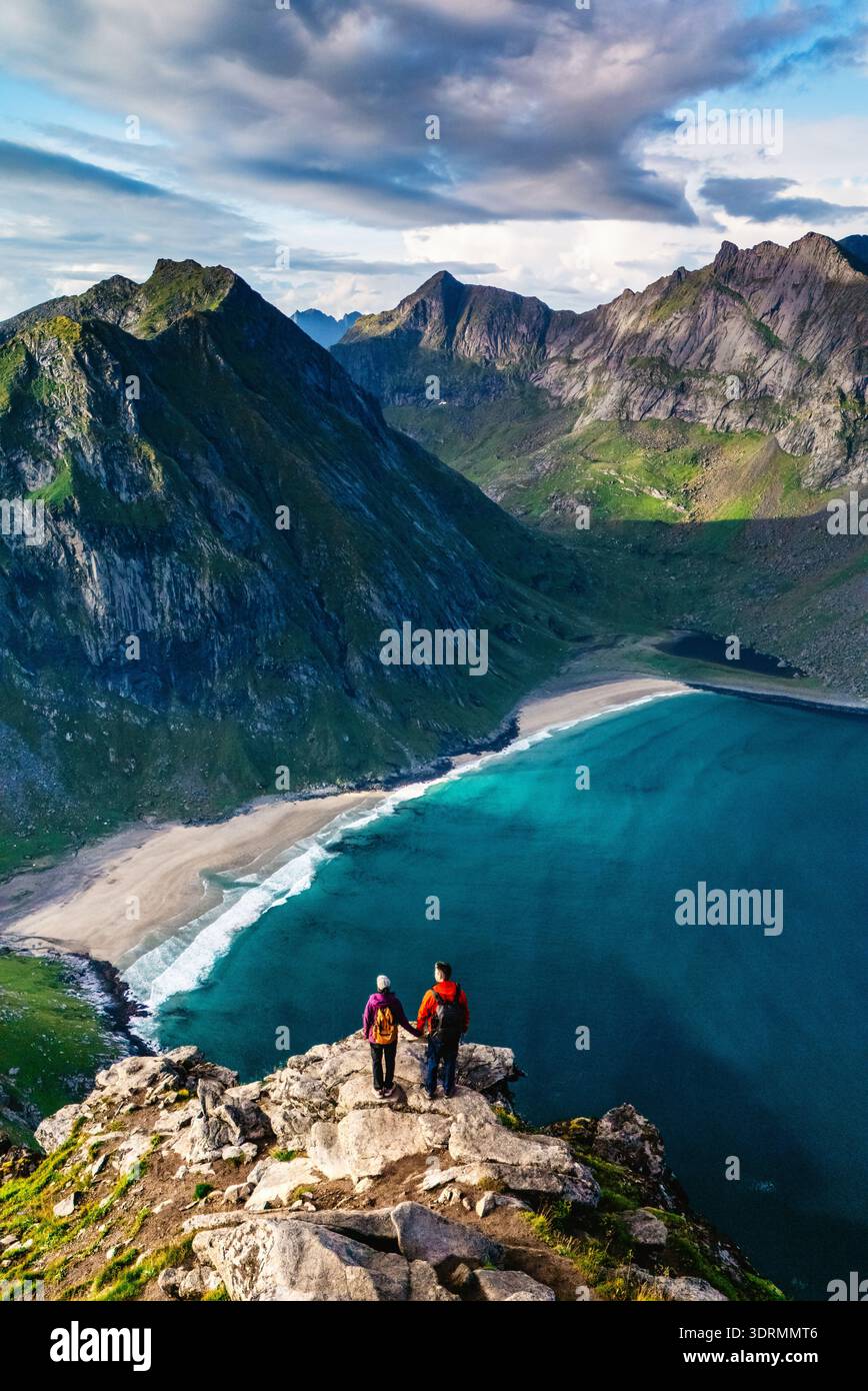 Les randonneurs profitent de vues époustouflantes depuis le sommet de Ryten sur le sentier de la plage de Kvalvika à Lofoten, en Norvège. L'eau turquoise sereine Banque D'Images