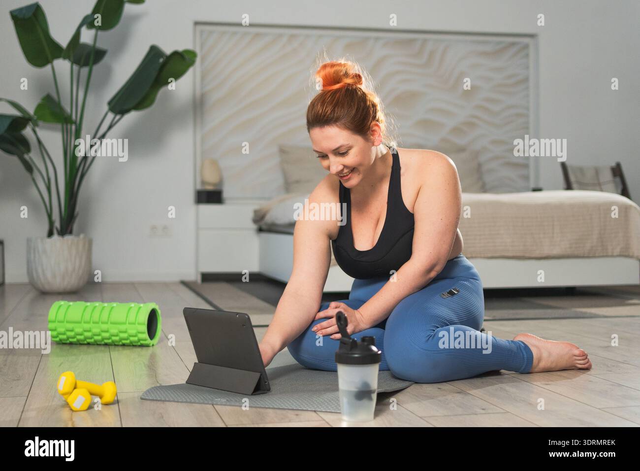Entraînement de yoga fitness en ligne. Femme pratiquant l'étirement avec des leçons d'application en ligne à la maison. Femme grande taille faisant du sport Banque D'Images
