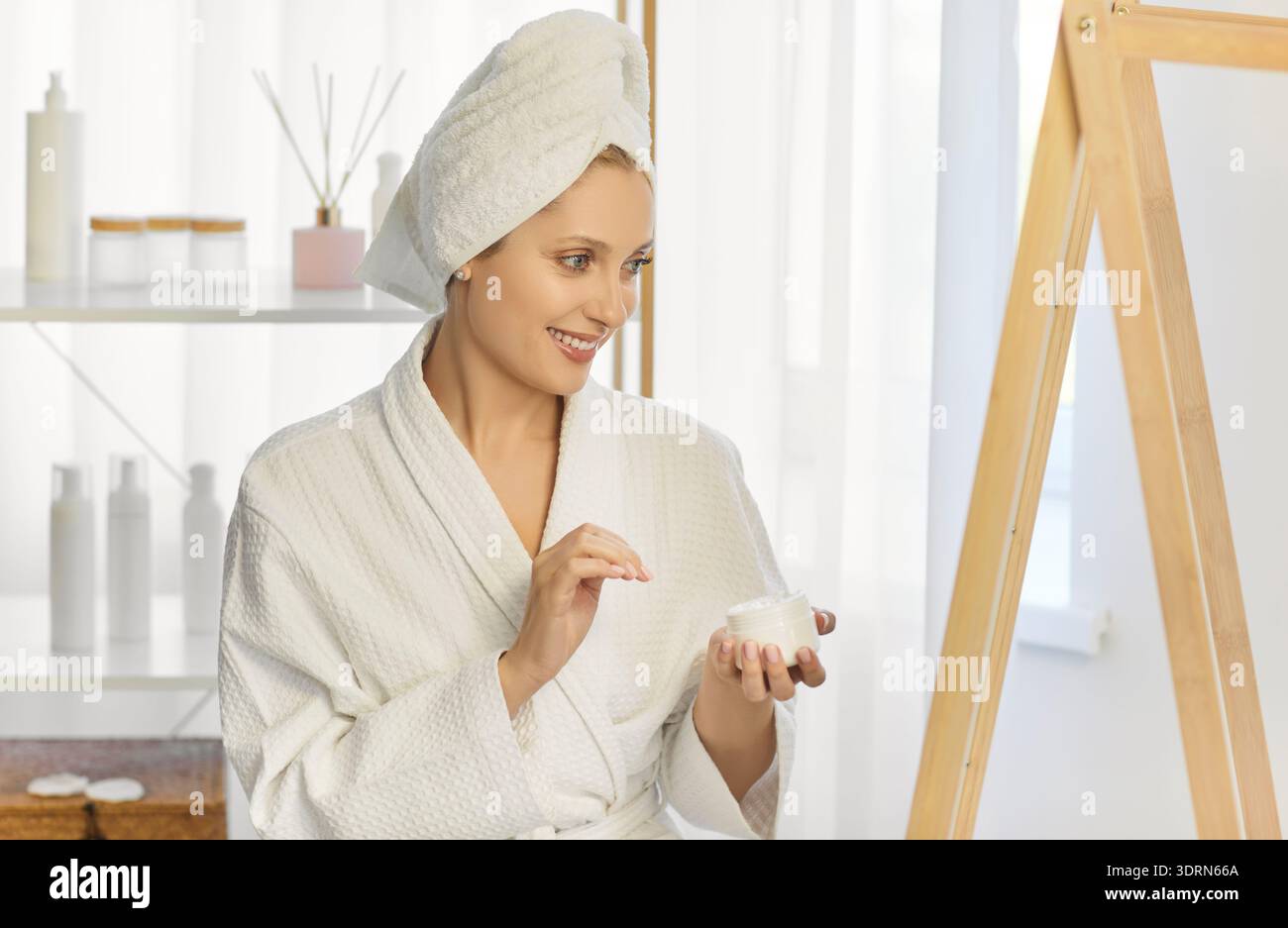 Belle femme portant un peignoir et une serviette enroulée autour de sa tête, regardant la crème petit pot Banque D'Images