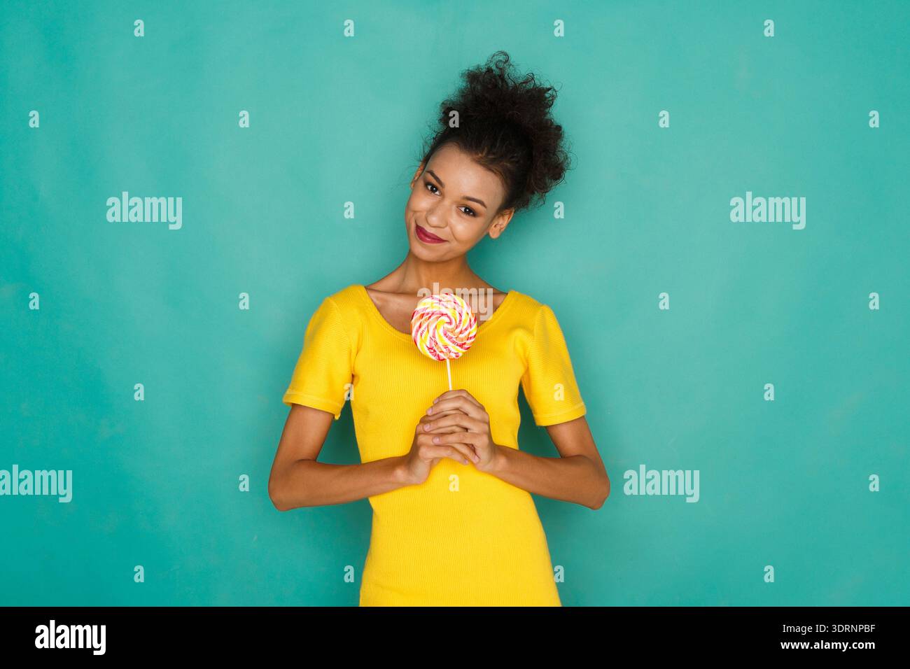 Femme tient Lollipop coloré en Bright Yellow Top sur fond Turquoise dans un cadre amusant Banque D'Images
