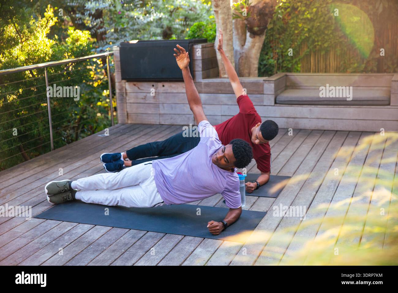 Hommes afro-américains effectuant des planches latérales sur la terrasse arrière avec tapis de yoga et bouteille d'eau. Fitness, bien-être, force, outdo Banque D'Images