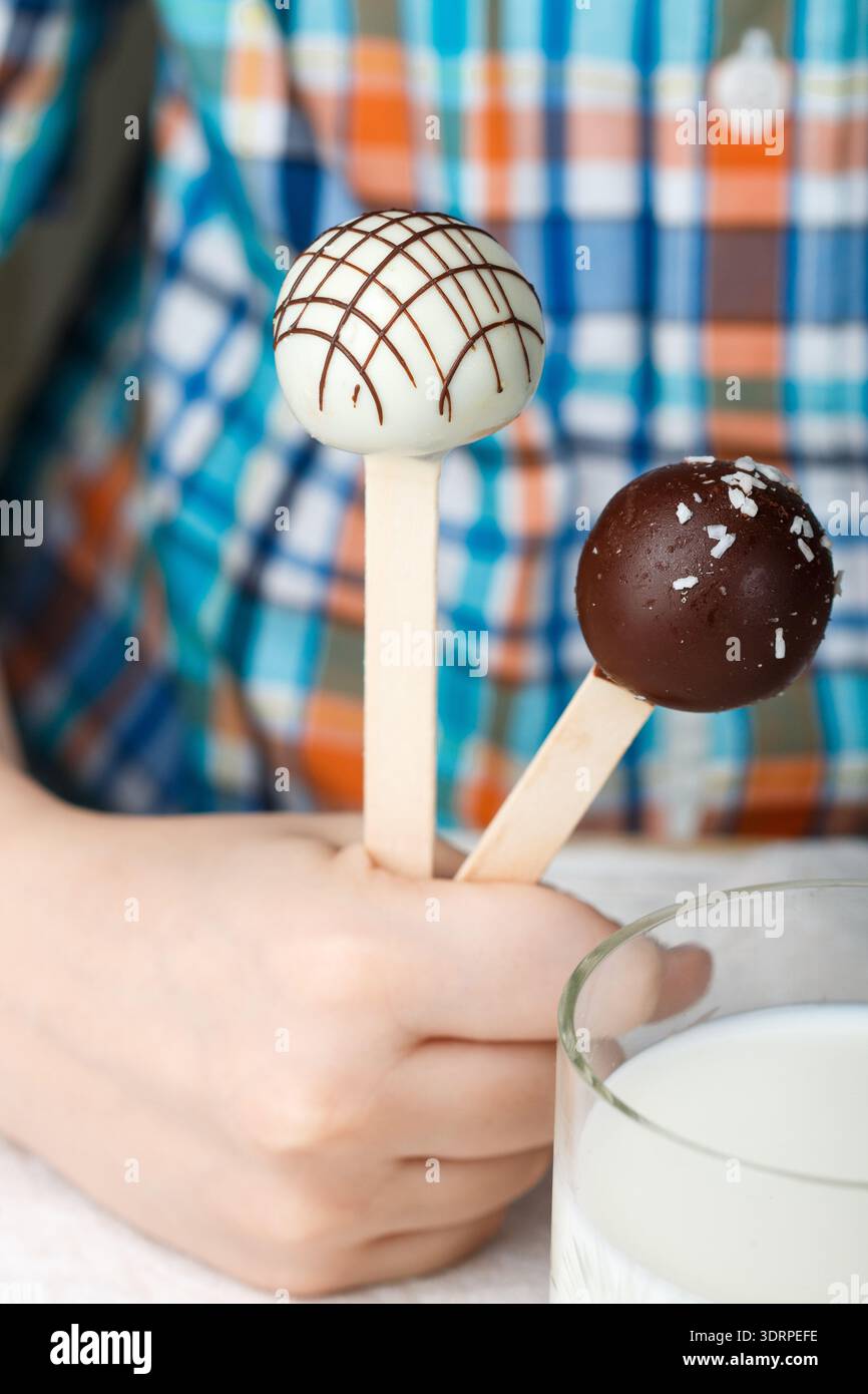 Deux cake pops décoré de chocolat blanc et noir dans les mains des enfants. Dessert pour les petits gourmets. Selective focus Banque D'Images