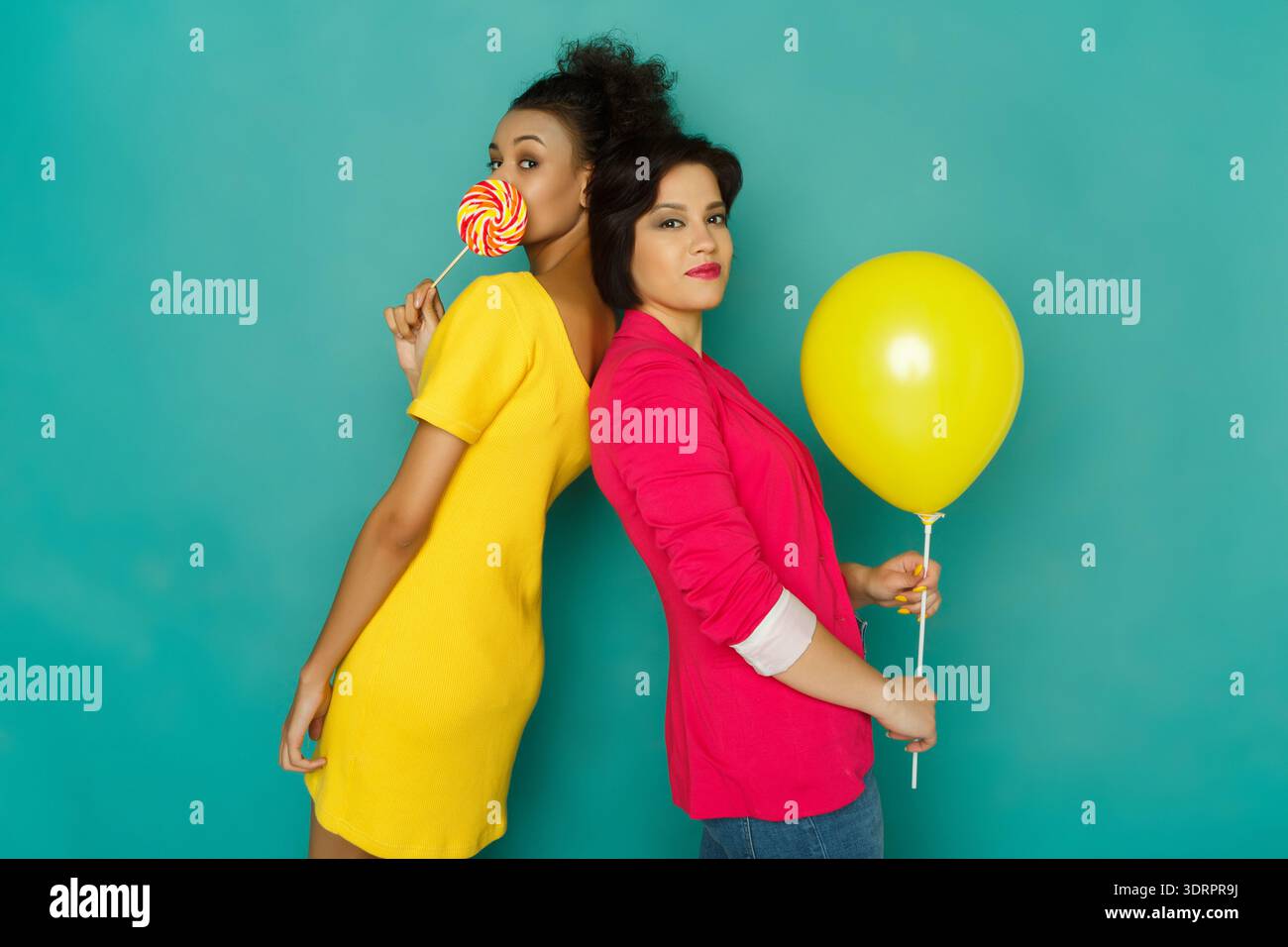 Deux femmes s'amusent avec une sucette et un ballon jaune sur fond bleu Banque D'Images