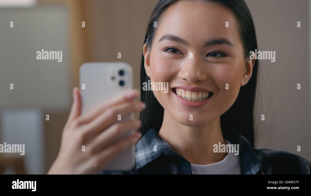 Heureuse asiatique fille coréenne femme souriante agitant la main parlant téléphone portable appel vidéo à la maison chinoise japonaise parlant webcam chat virtuel en ligne Banque D'Images