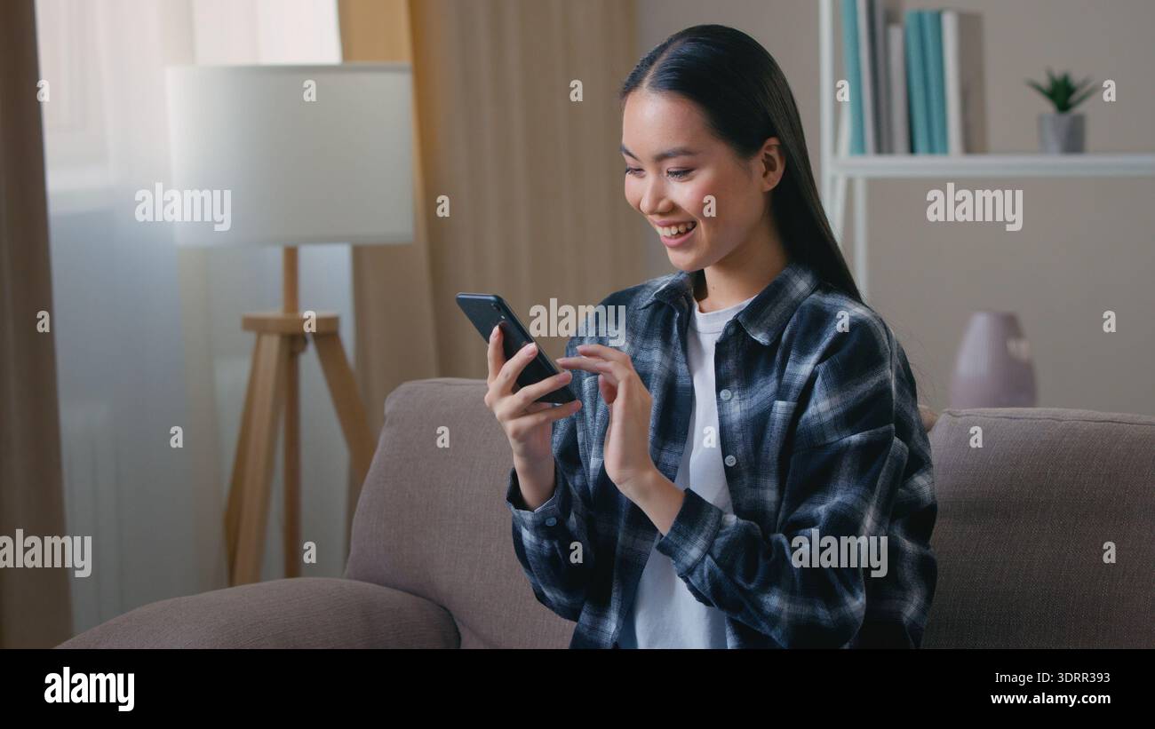 Kharkiv, Ukraine - 24.12.2021 : femme coréenne asiatique souriante à l'aide d'un smartphone à la maison chat en ligne fille femme commandant un service de réservation de livraison Banque D'Images