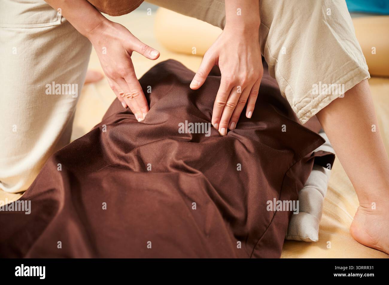 Masseuse faisant massage yoga thaïlandais. Fermez le thérapeute de la main de la femme faisant le traitement de massage traditionnel pour la patiente à l'intérieur. Client allongé sur tapis, profitant d'un massage des mains dans une atmosphère calme. Banque D'Images