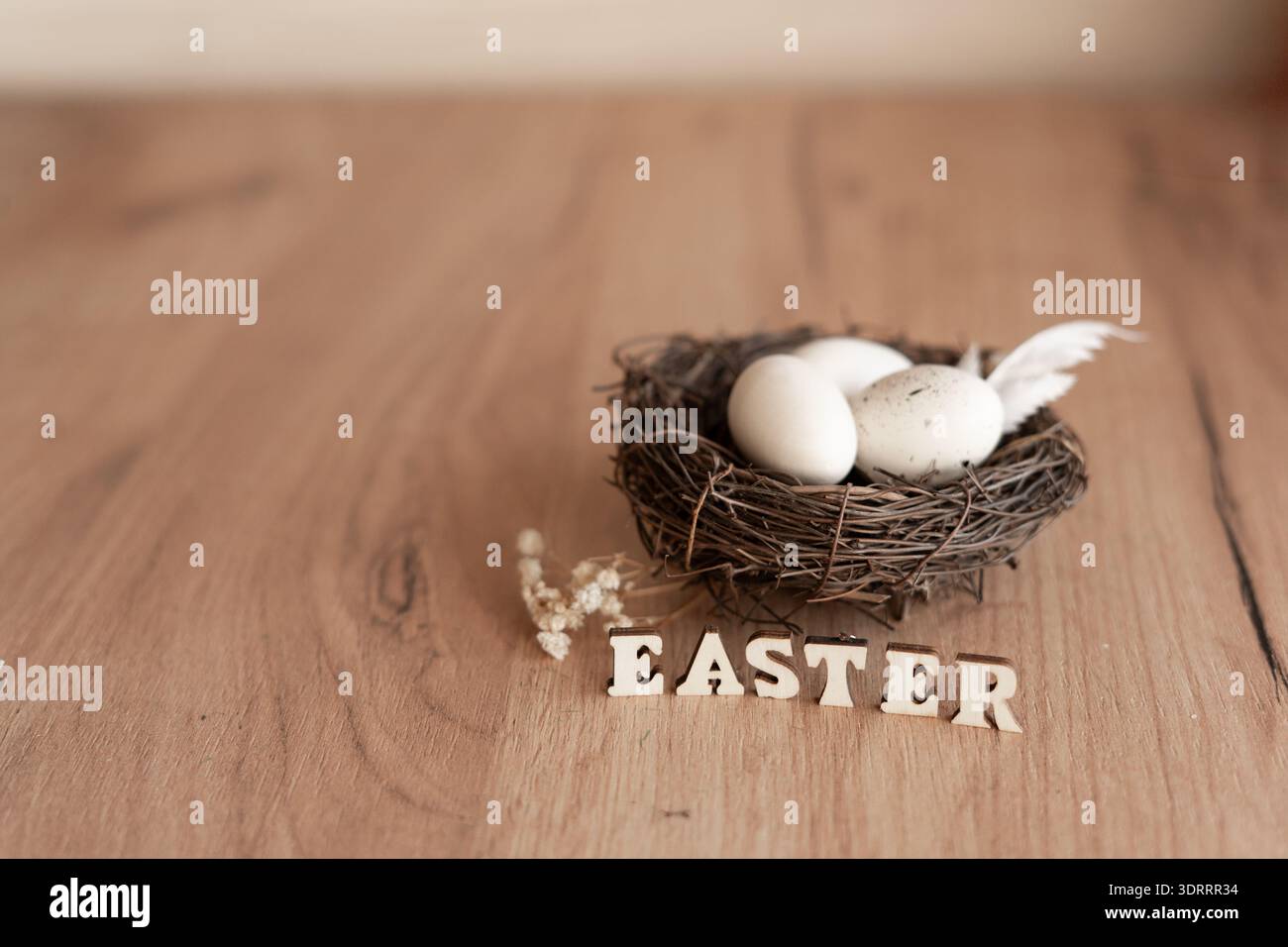 Nid de Pâques avec des œufs blancs et des lettres en bois sur une table rustique. Nid d'oiseau de nature morte de Pâques minimal avec des œufs blancs et des plumes sur une table en bois rustique Banque D'Images