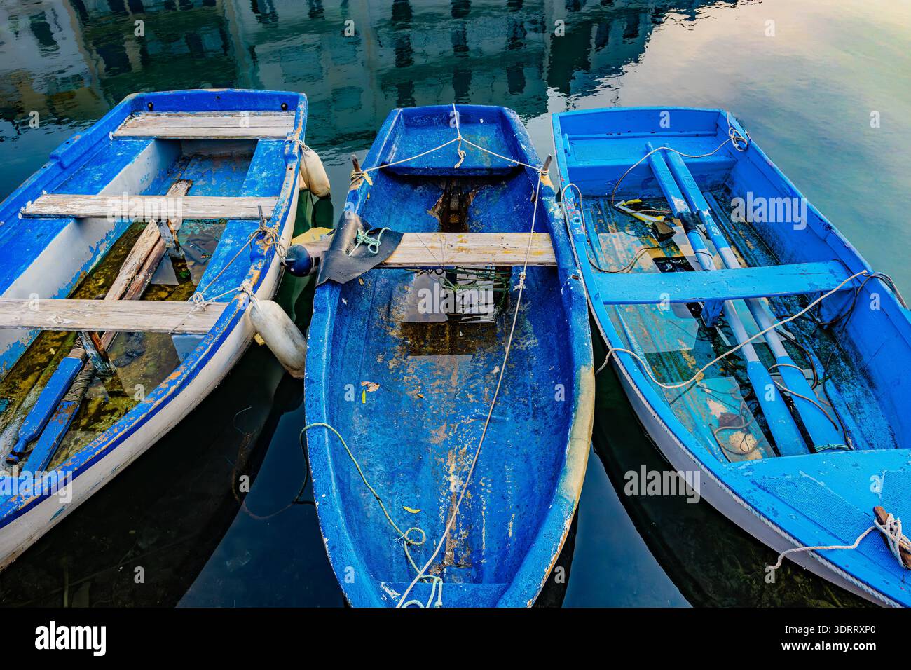 L’Ametlla de Mar, Espagne – trois bateaux de pêche bleus en bois amarrés ensemble dans les eaux calmes du port reflétant les bâtiments voisins Banque D'Images