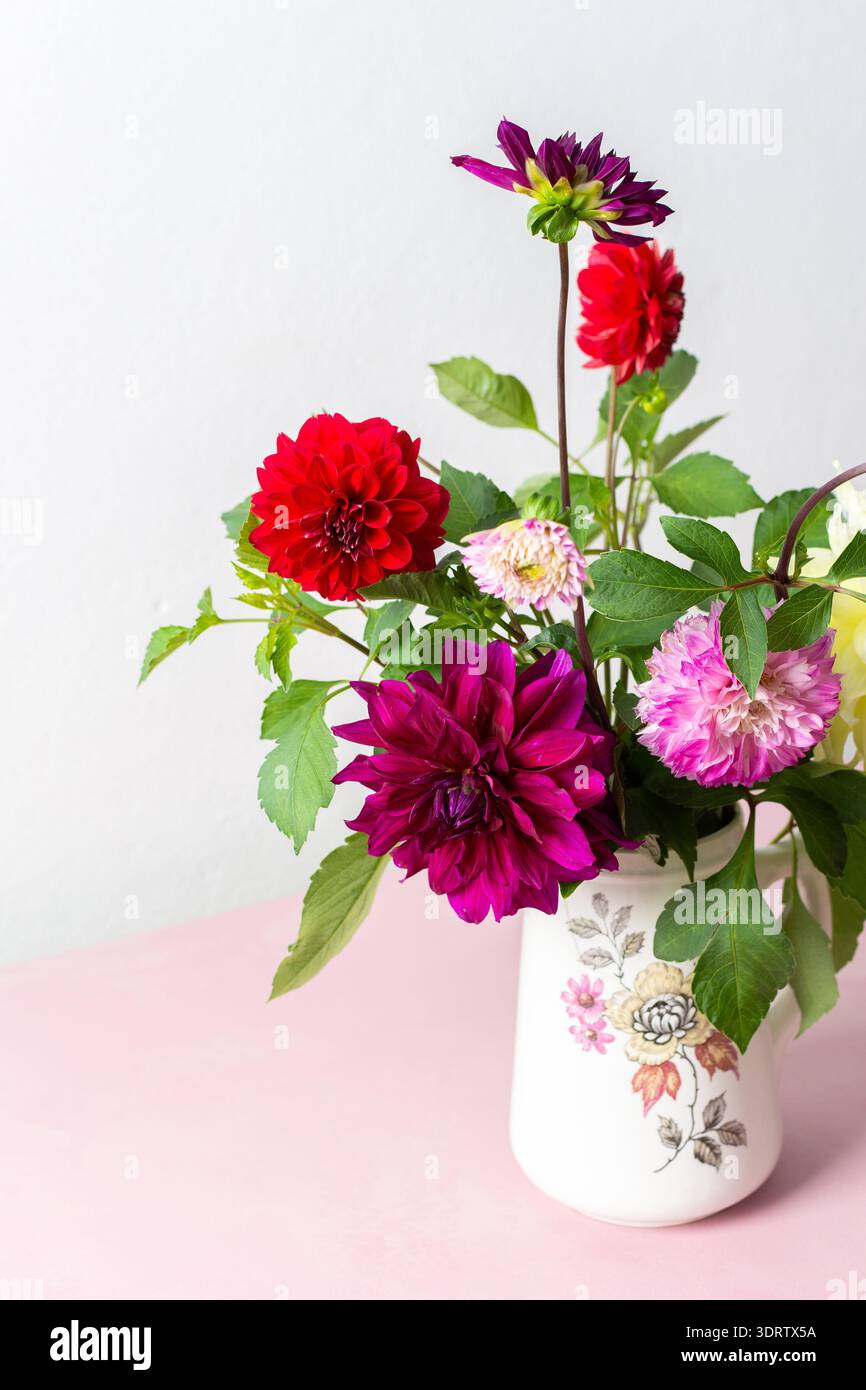 Un vase contient une variété de fleurs fraîches avec différentes couleurs. Les fleurs sont placées sur une table rose. Derrière le vase se trouve un mur Uni dans un roo lumineux Banque D'Images