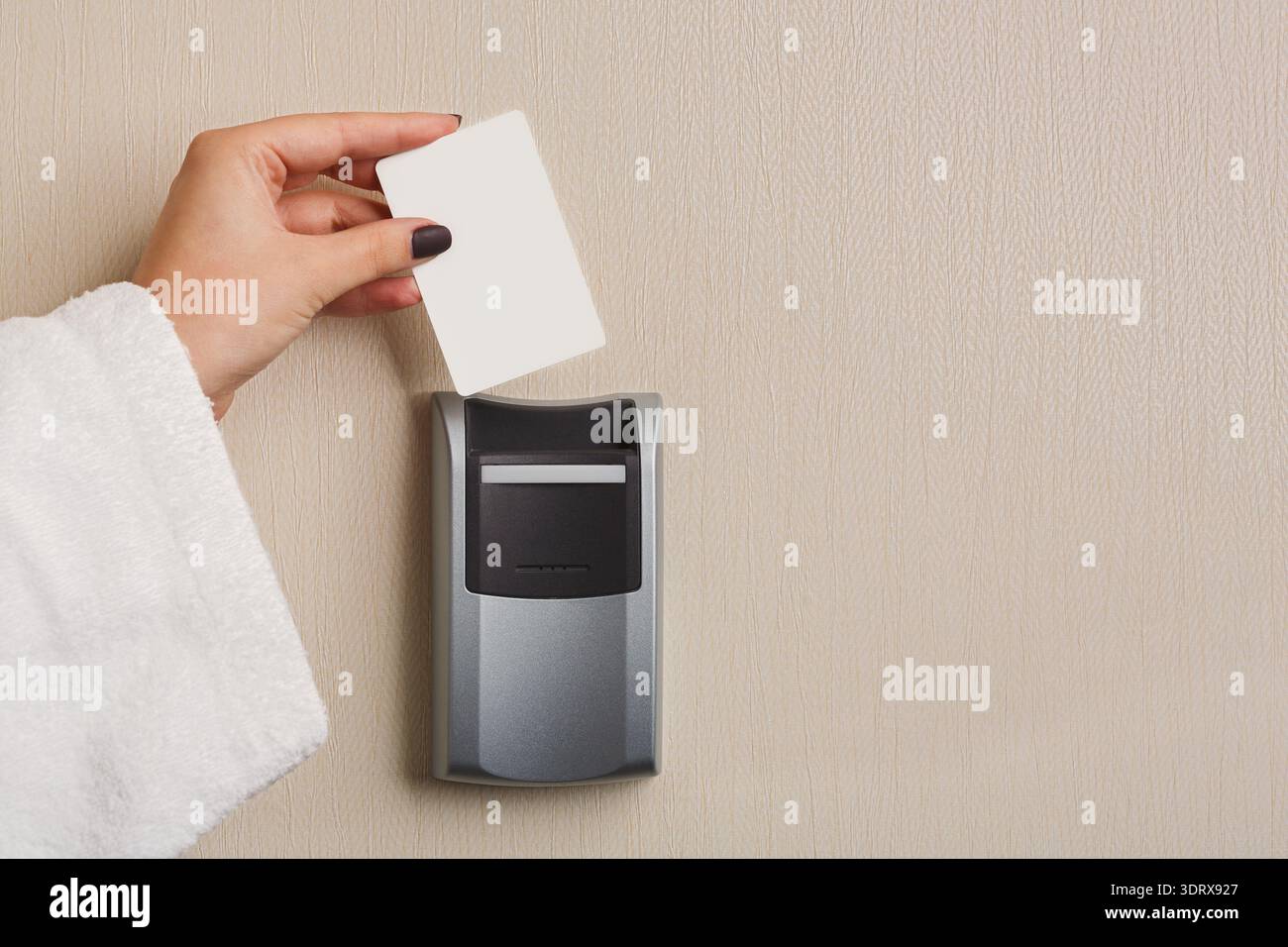 Main tenant une carte-clé près d'un lecteur de carte sur un mur dans une chambre d'hôtel Banque D'Images