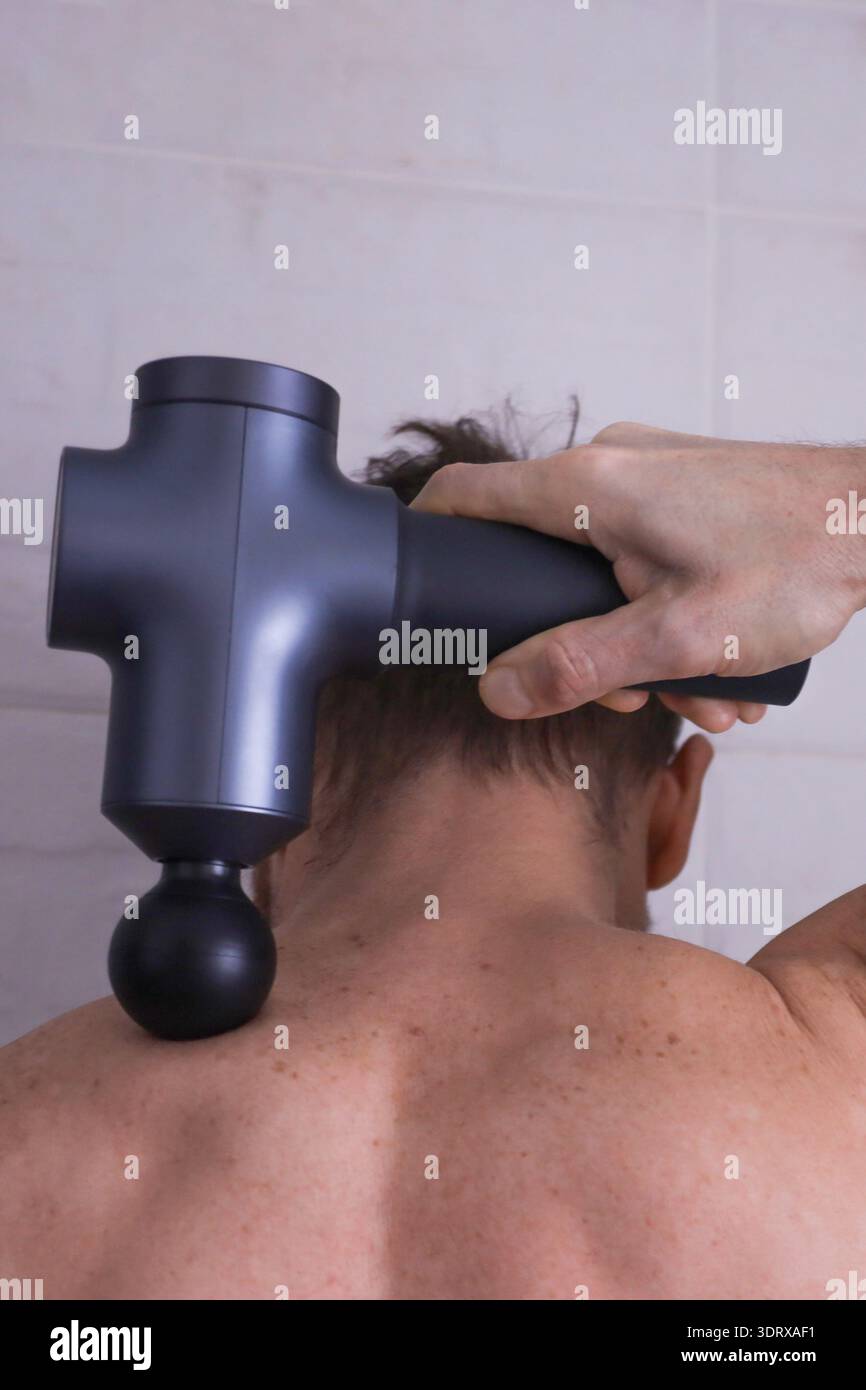 Gros plan vue arrière de l'homme utilisant le pistolet de massage à percussion sur la zone du col cervical pour la relaxation musculaire profonde Banque D'Images