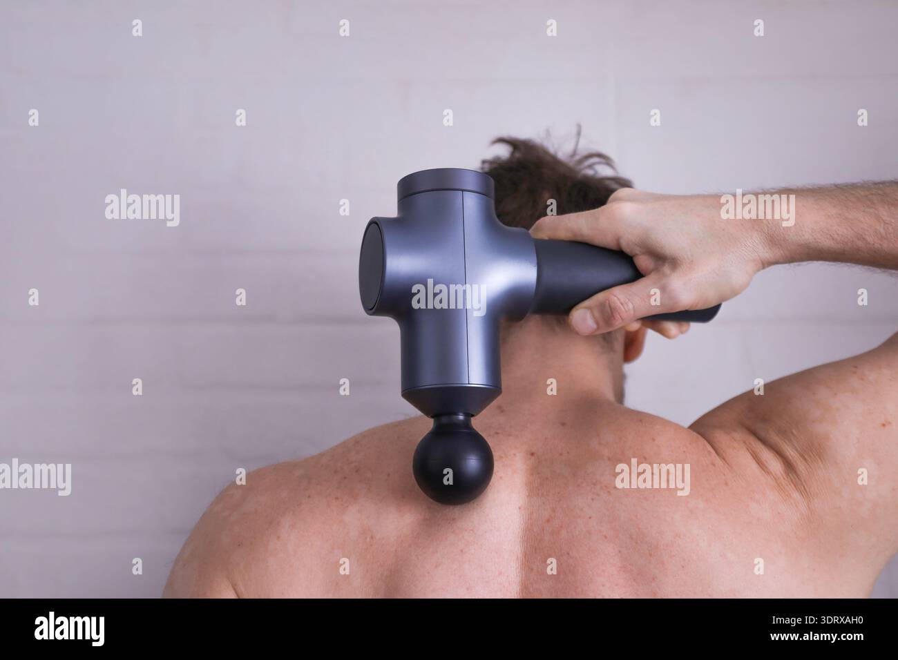 Vue arrière rapprochée de l'homme utilisant un masseur à percussion sur la zone du col cervical avec espace de copie pour la santé ou le message de forme physique Banque D'Images