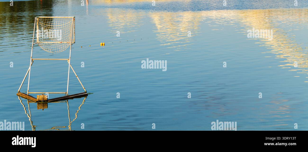 Un but de water-polo solitaire flotte sur une eau bleue sereine, reflétant les teintes chaudes du soleil couchant Banque D'Images