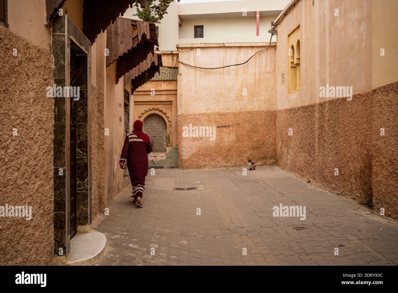 Une vue arrière saisissante d'une femme portant une djellaba Bourgogne alors qu'elle marche le long d'une rue calme au cœur de la médina de Meknès, une HE mondiale de l'UNESCO Banque D'Images