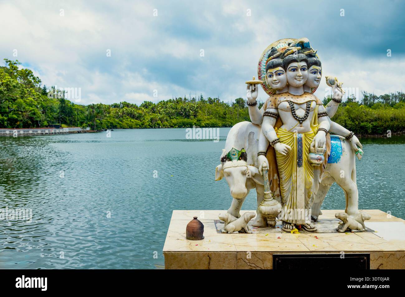 Statue du Seigneur Shiva avec plusieurs têtes et bras debout à côté d'une vache sacrée près d'un lac Banque D'Images