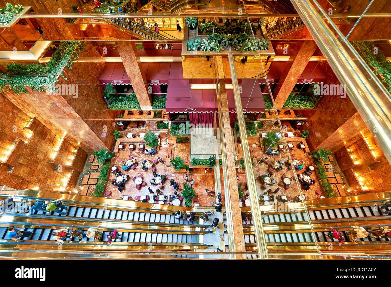 Les gens s'assoient et parlent dans l'atrium de la Trump Tower tandis que certains marchent dans les escaliers. L'espace a de nombreuses plantes et surfaces réfléchissantes. Banque D'Images