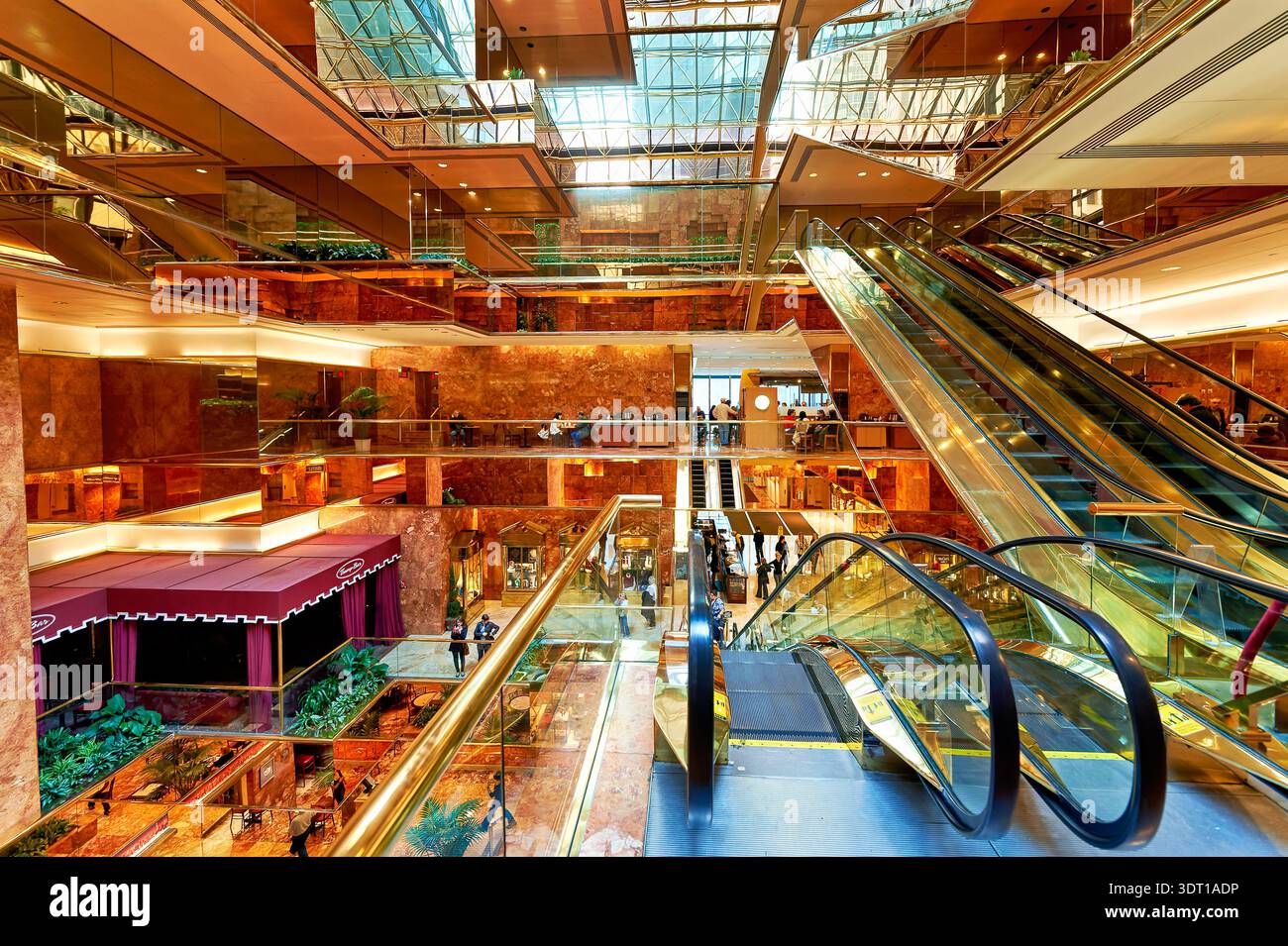 Les gens marchent et interagissent dans l’atrium de la Trump Tower tandis que les escaliers mécaniques montent et descendent. L'espace dispose de grands murs et de grandes fenêtres. Banque D'Images