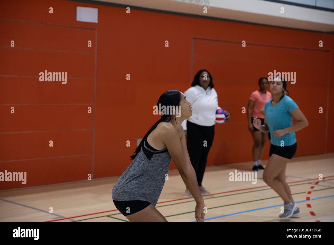 Diverses coéquipières féminines pratiquant le volley-ball dans le gymnase en vêtements de sport avec entraîneur tenant le volley-ball Banque D'Images