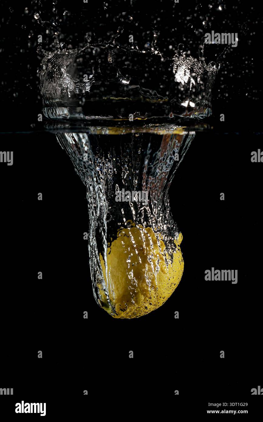 Un citron tombe dans un récipient d'eau, soulevant une très grande éclaboussure Banque D'Images