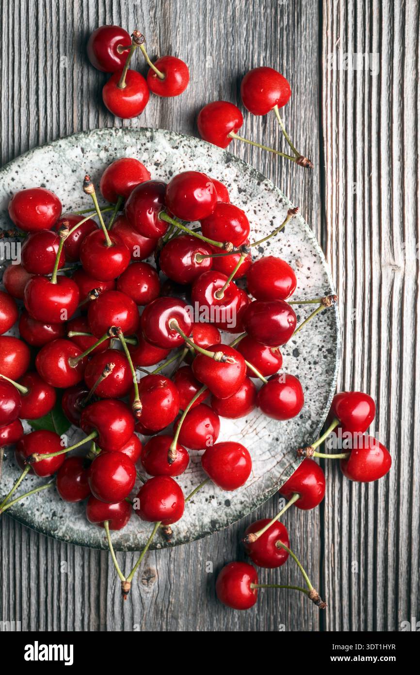 Vue de dessus de cerises mûres dispersées sur fond de bois. Fruits sucrés rouge vif, concept de récolte saisonnière Banque D'Images