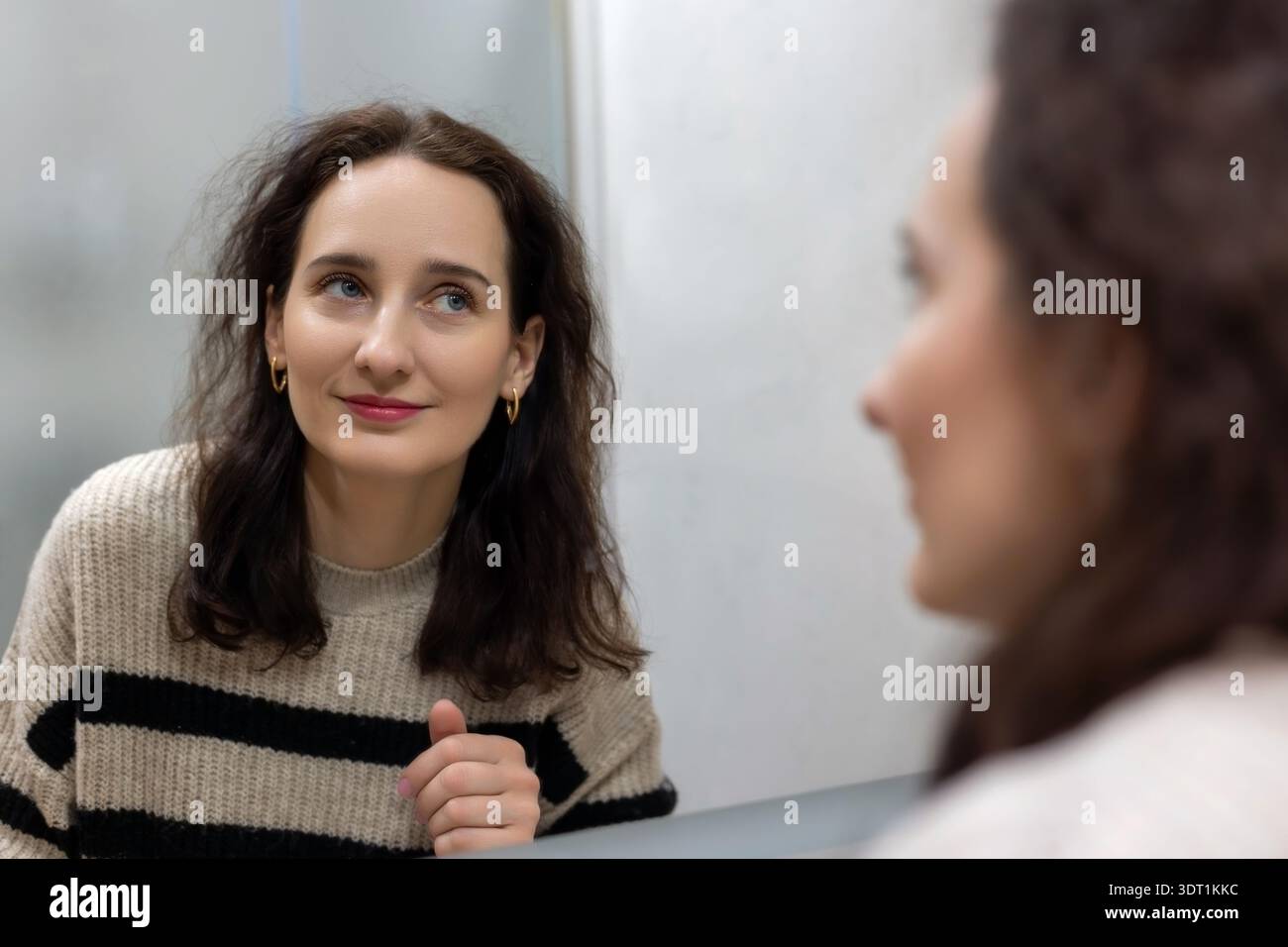 Femme d'âge moyen souriant à la réflexion du miroir de la salle de bain. Portrait en gros plan d'une femme brune d'âge moyen regardant son reflet dans une salle de bain Banque D'Images