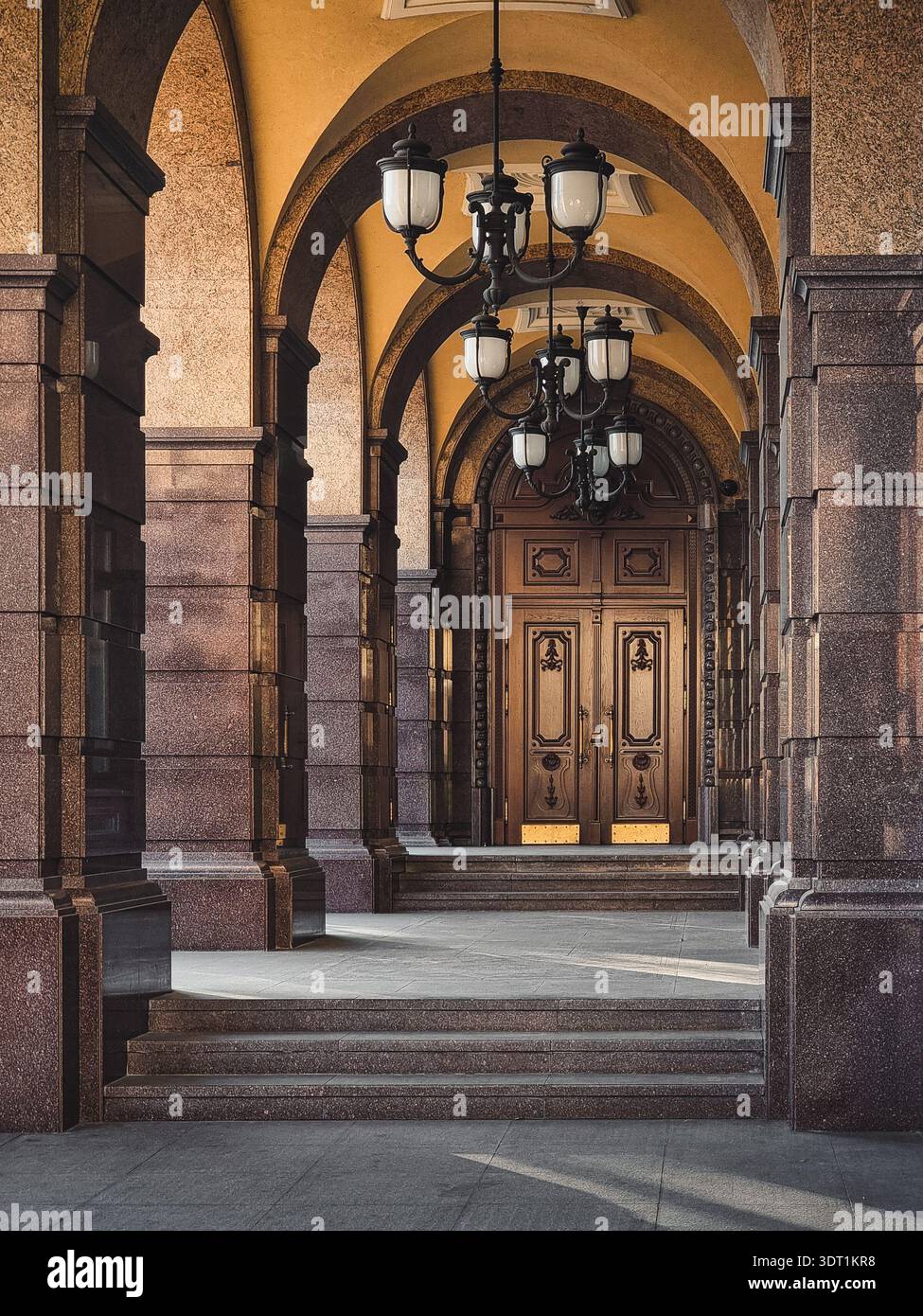 Colonnade voûtée avec lustres ornés menant à une grande porte. Passerelle architecturale avec piliers en pierre, arcs voûtés et lustres noirs ornés Banque D'Images