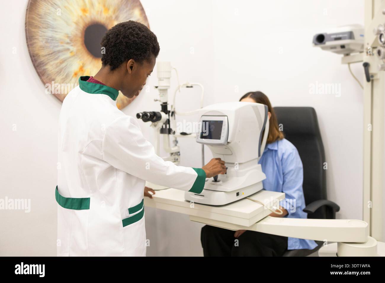Un opticien effectue un examen visuel détaillé à l'aide d'un équipement de pointe, aidant un patient assis à proximité. Le bureau présente un grand œil artistique Banque D'Images