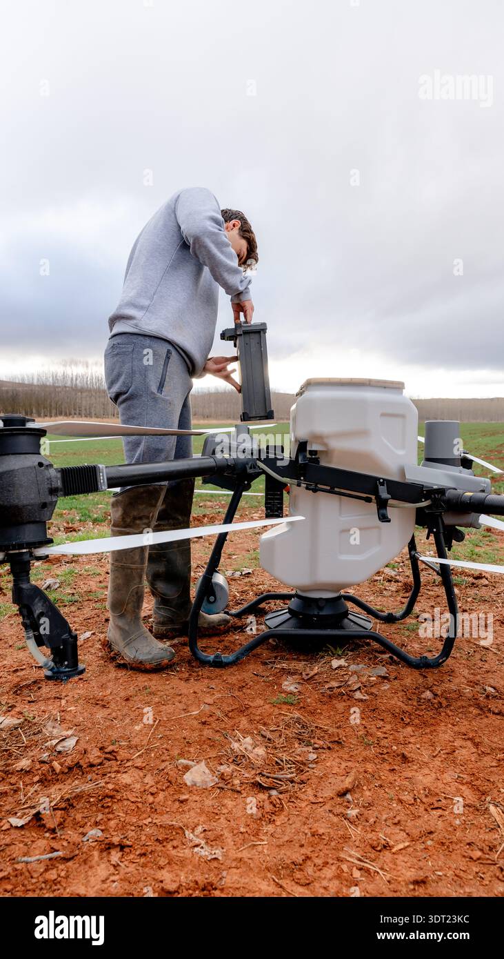 Un technicien en tenue grise répare le système de batterie d'un gros drone agricole dans un champ ouvert. La scène capture l'intersection de technolo Banque D'Images