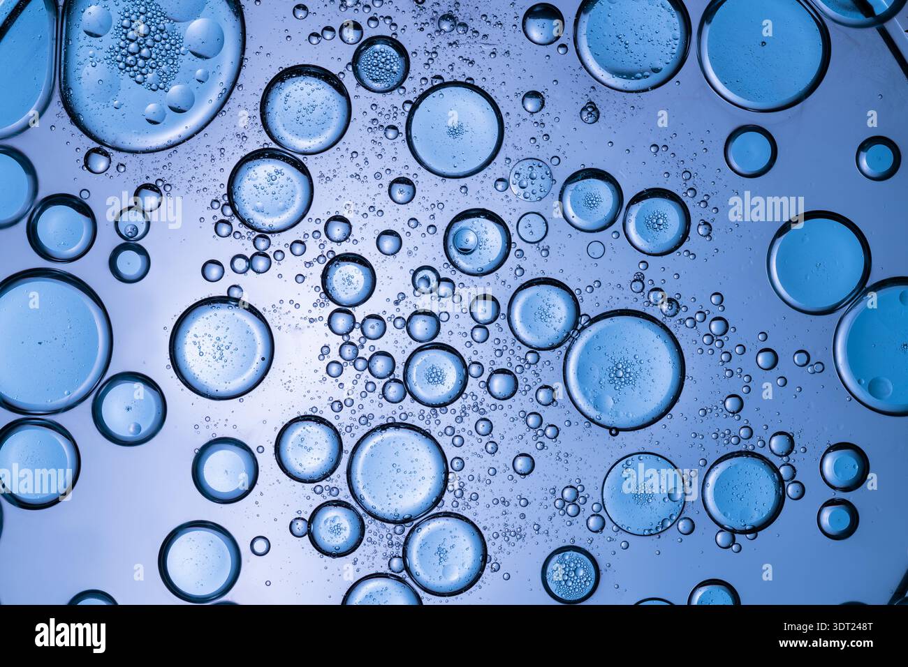 Macro photographie de bulles bleues de tailles variables sur une surface liquide, créant un fond texturé et complexe. Les détails en gros plan soulignent la Banque D'Images