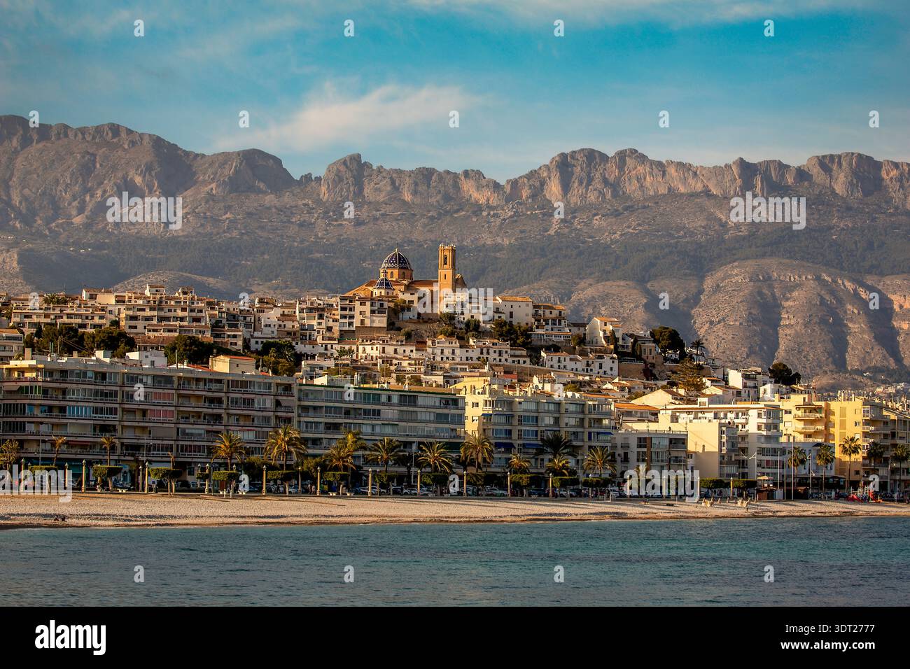 Une ville côtière ensoleillée avec des bâtiments blancs à flanc de colline, une église en forme de dôme, plage bordée de palmiers, Altea, Espagne Banque D'Images