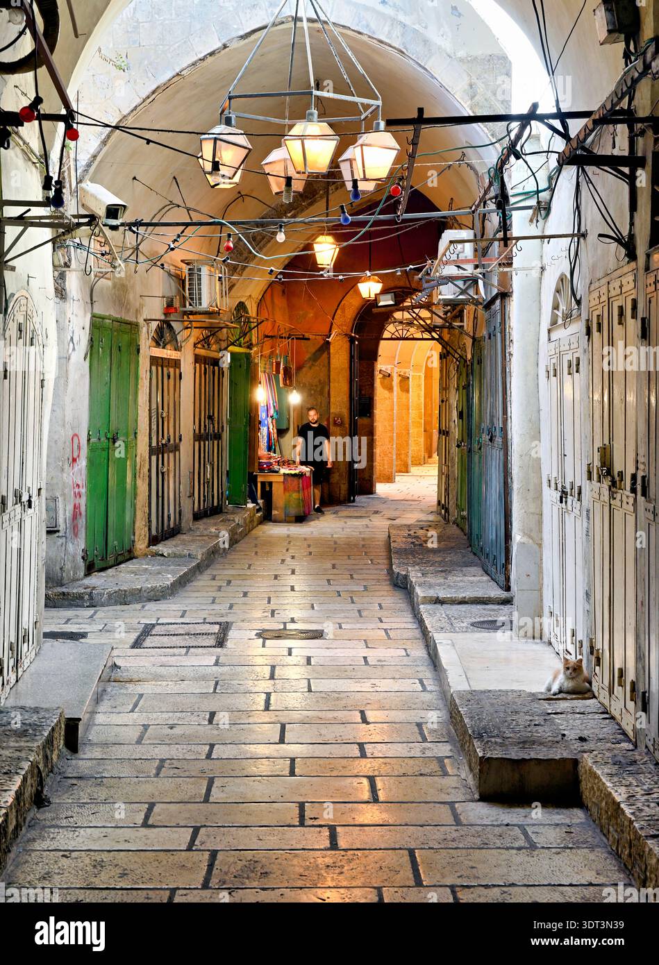 Une rue pavée dans la vieille ville de Jérusalem mène à des magasins et à un vendeur. Les gens se promènent dans le quartier historique, entouré de murs de pierre. Banque D'Images