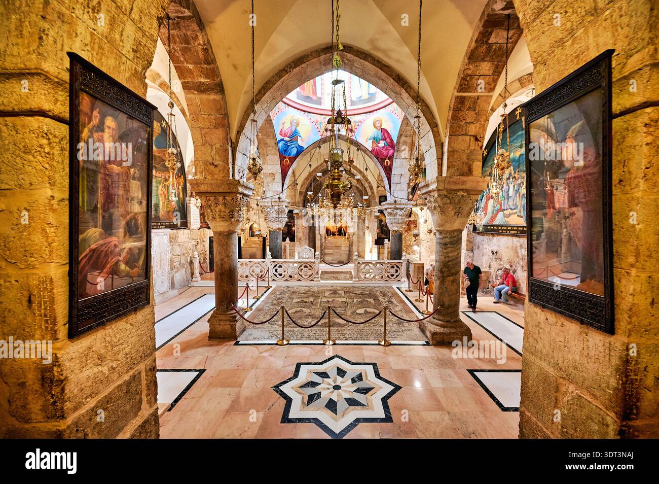 Les gens marchent à l'intérieur de l'église du Saint-Sépulcre à Jérusalem. L'espace a de grandes arches et des œuvres d'art sur les murs. Banque D'Images