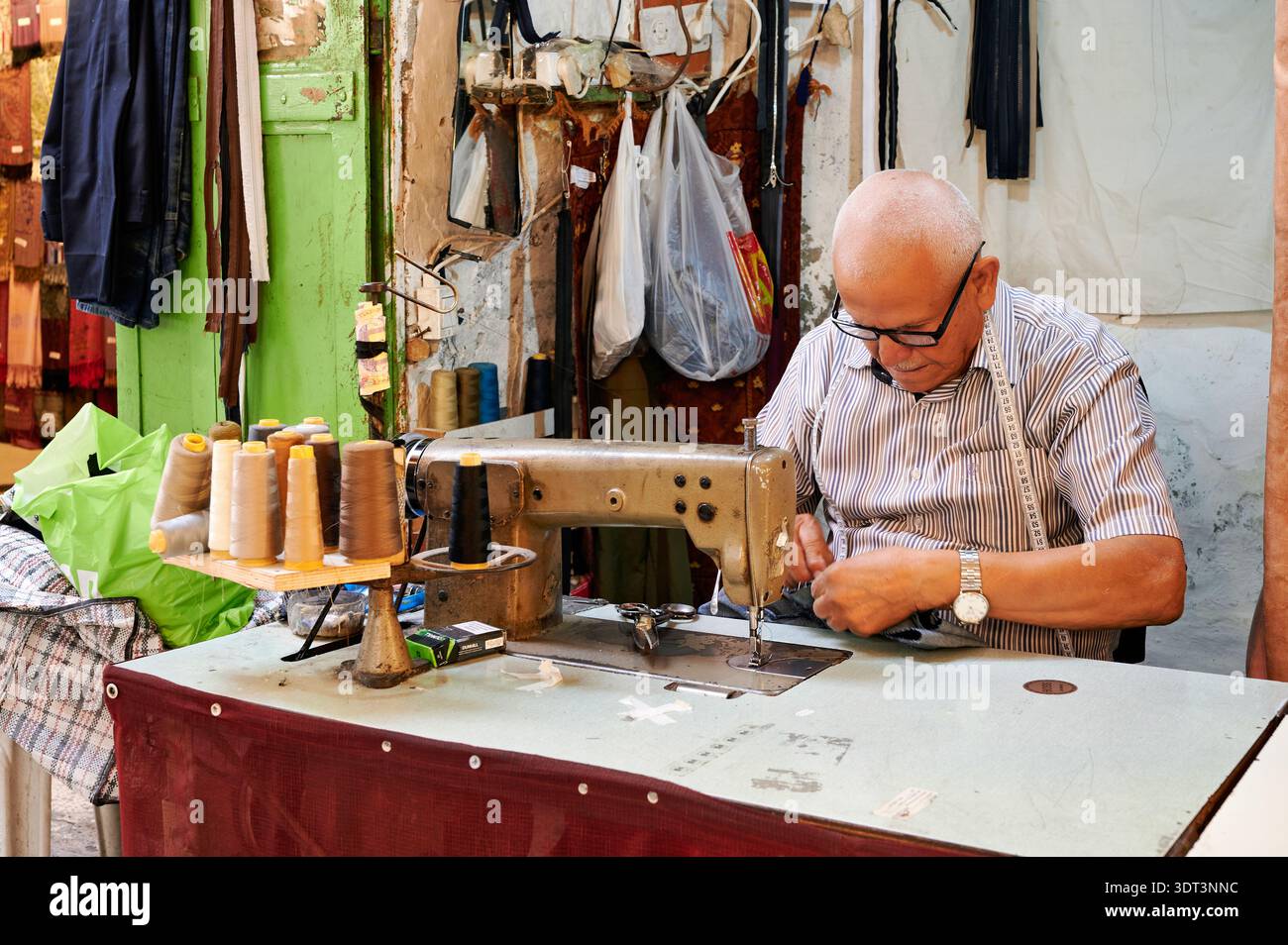 Un tailleur coud du tissu dans le quartier juif de Jérusalem. La boutique a des fils et des matériaux autour de lui. Banque D'Images
