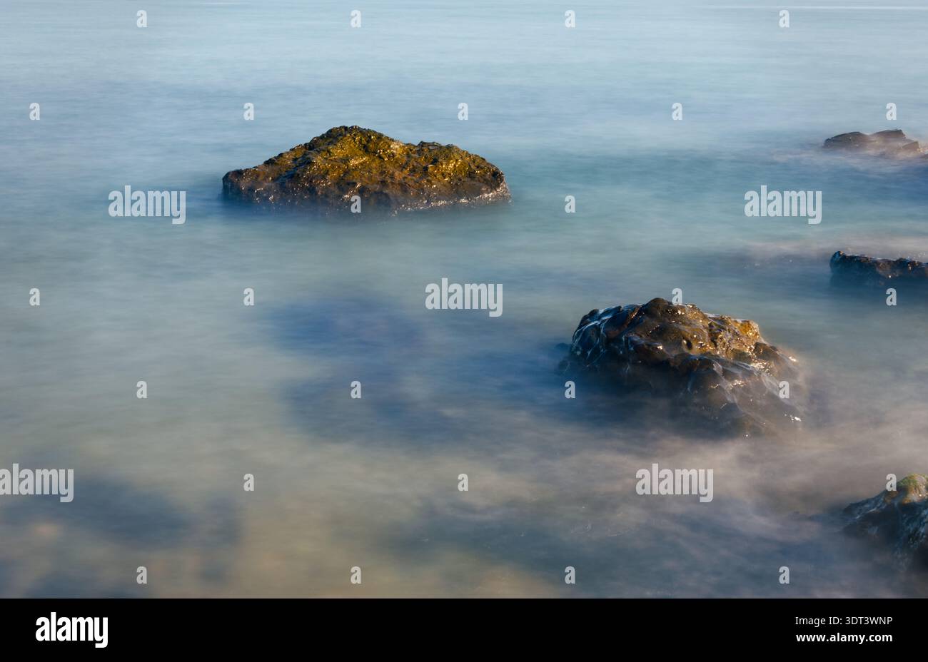 Gros plan longue exposition de vagues de mer s'écrasant au-dessus de pierres. Une photo détaillée à longue exposition montrant le mouvement soyeux de l'eau autour de roches sombres. Le Banque D'Images