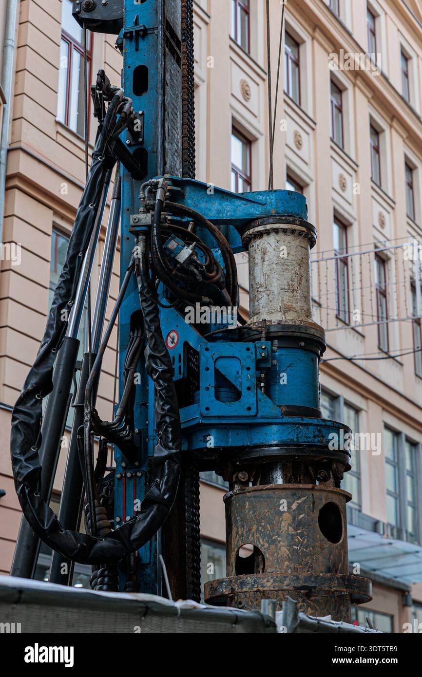 Engin de forage bleu et machinerie de construction lourde installé contre un bâtiment historique de la ville, montrant des équipements industriels, des tuyaux hydrauliques et du weat Banque D'Images