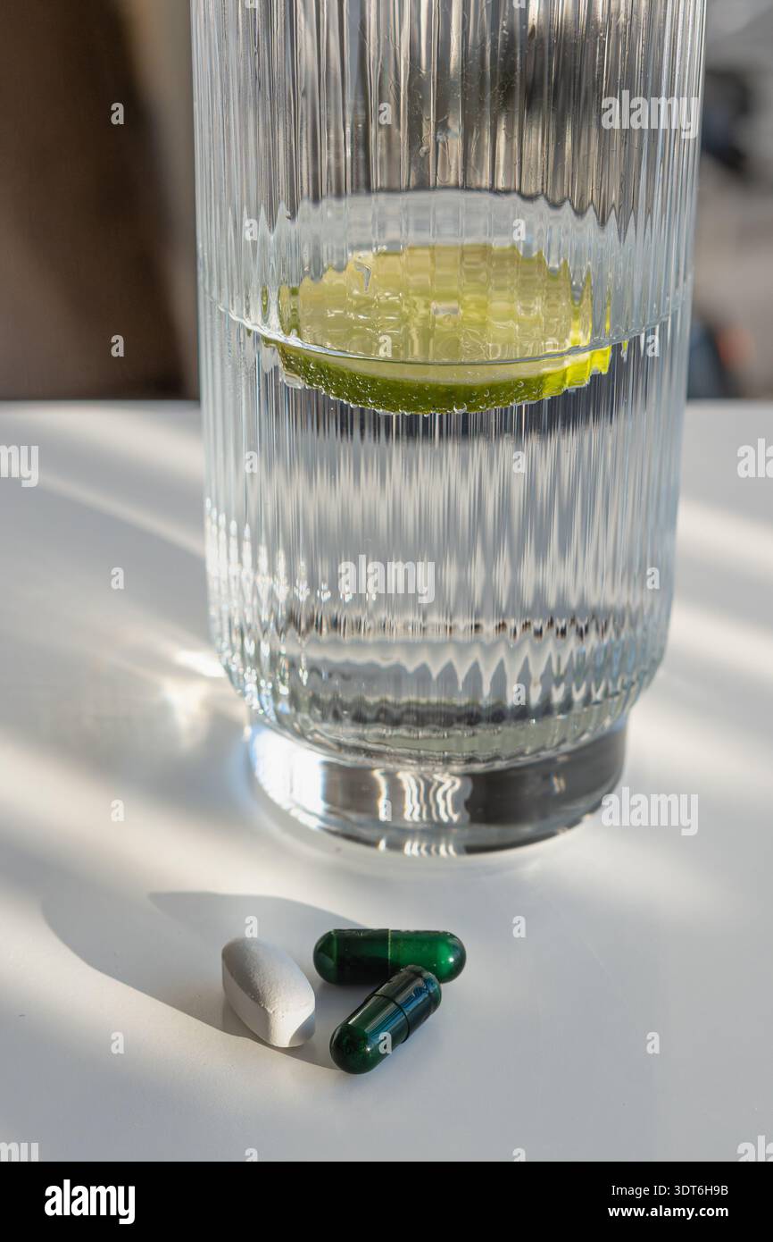 Comprimés et capsules colorés assortis dans une mise au point nette, avec un verre d'eau infusée de chaux et de glace, soins de santé, médicaments quotidiens, apport en vitamines Banque D'Images