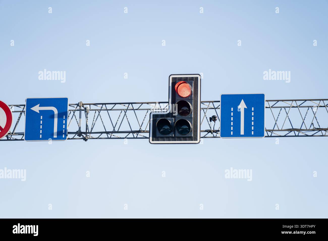 Gros plan des panneaux de contrôle de la circulation surélevés sur une ferme métallique, avec un feu stop rouge, un panneau d'interdiction de demi-tour et des flèches de voie pour les routes droites et à gauche Banque D'Images