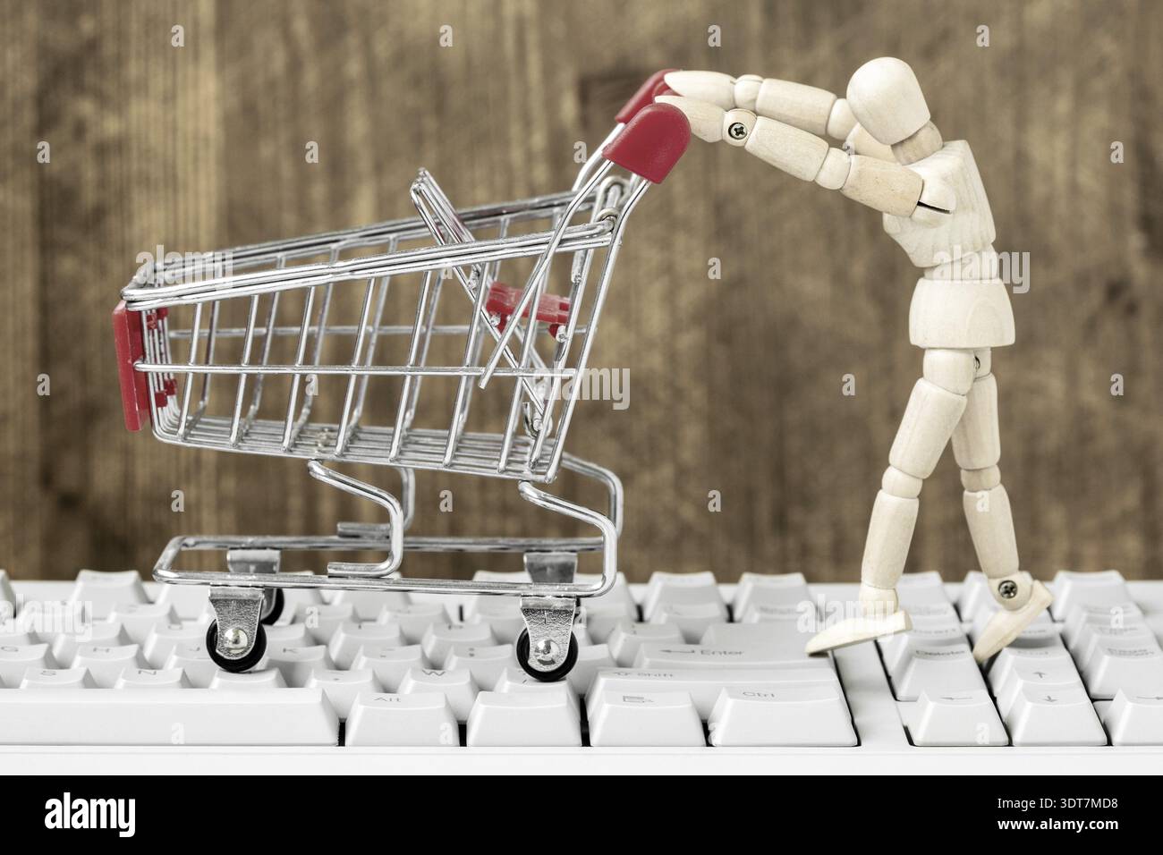 Mannequin en bois poussant le chariot vide sur le clavier de l'ordinateur. Concept d'achat en ligne. E-commerce Banque D'Images