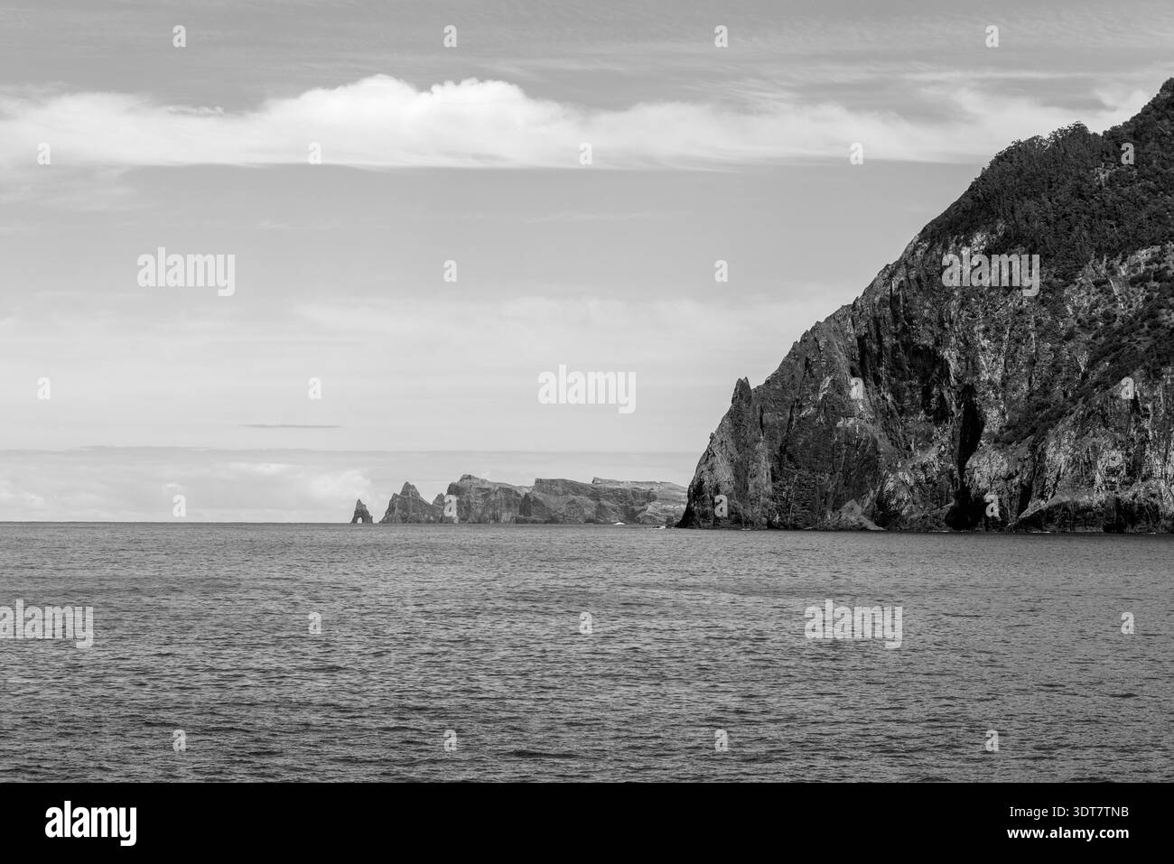Paysage monochrome de falaises et d'îlots de roche à Porto da Cruz Madeira, eau calme de l'Atlantique et nuages en couches s'étendant au-dessus d'une pointe rocheuse accidentée. Banque D'Images