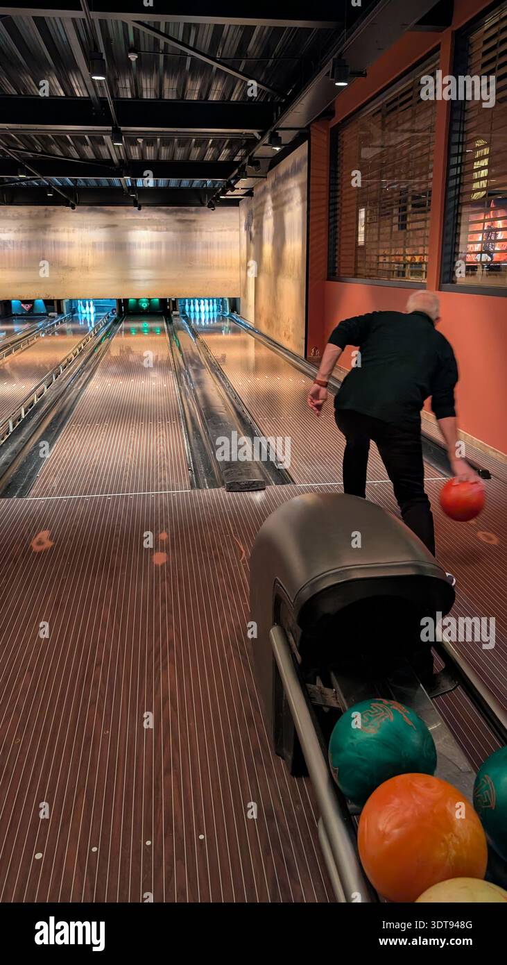 Man Bowling dans Une piste de bowling intérieure rétro Rolling an Orange Ball Down Wooden Lanes Banque D'Images