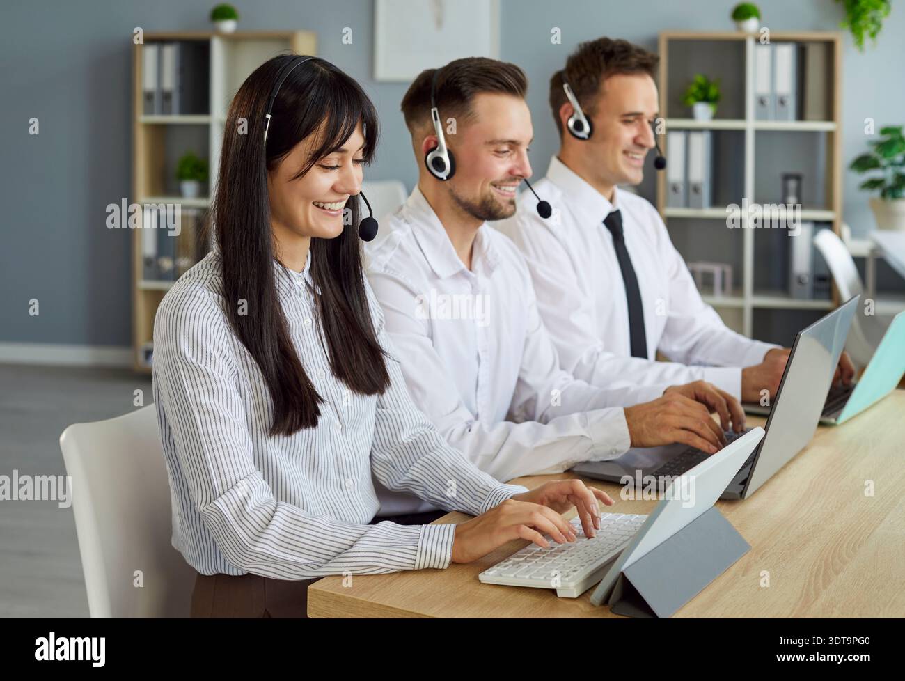 Équipe de service client masculin et féminin avec des micro-casques/oreillettes fonctionnant sur des ordinateurs portables Banque D'Images