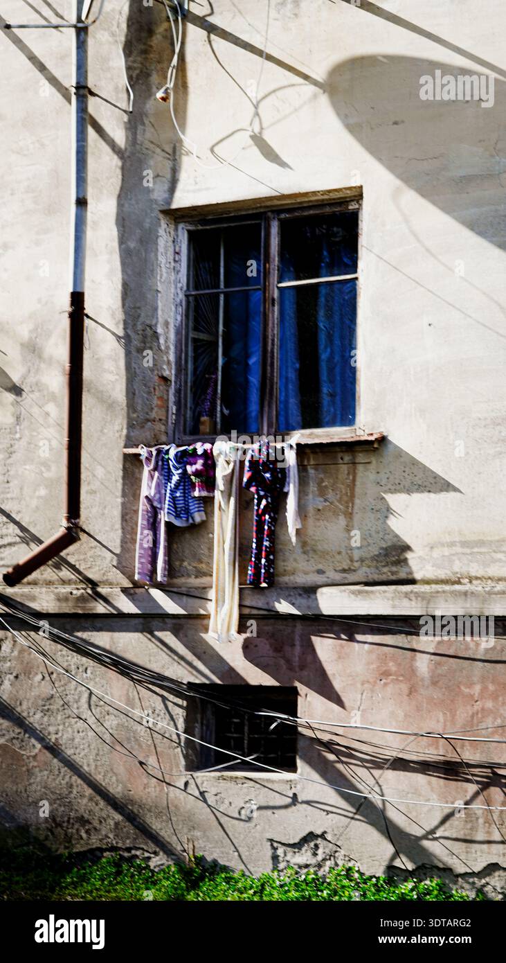 Séchage des vêtements sur une ligne à l'extérieur d'une fenêtre d'un bâtiment vieilli avec de la peinture pelable et des fils Banque D'Images