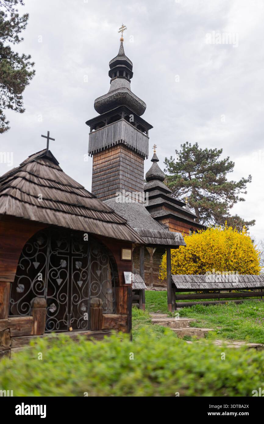 Église historique en bois avec architecture ukrainienne traditionnelle et bardeaux en bois. Paysage de printemps avec buisson jaune fleuri et ciel nuageux. Cultura Banque D'Images