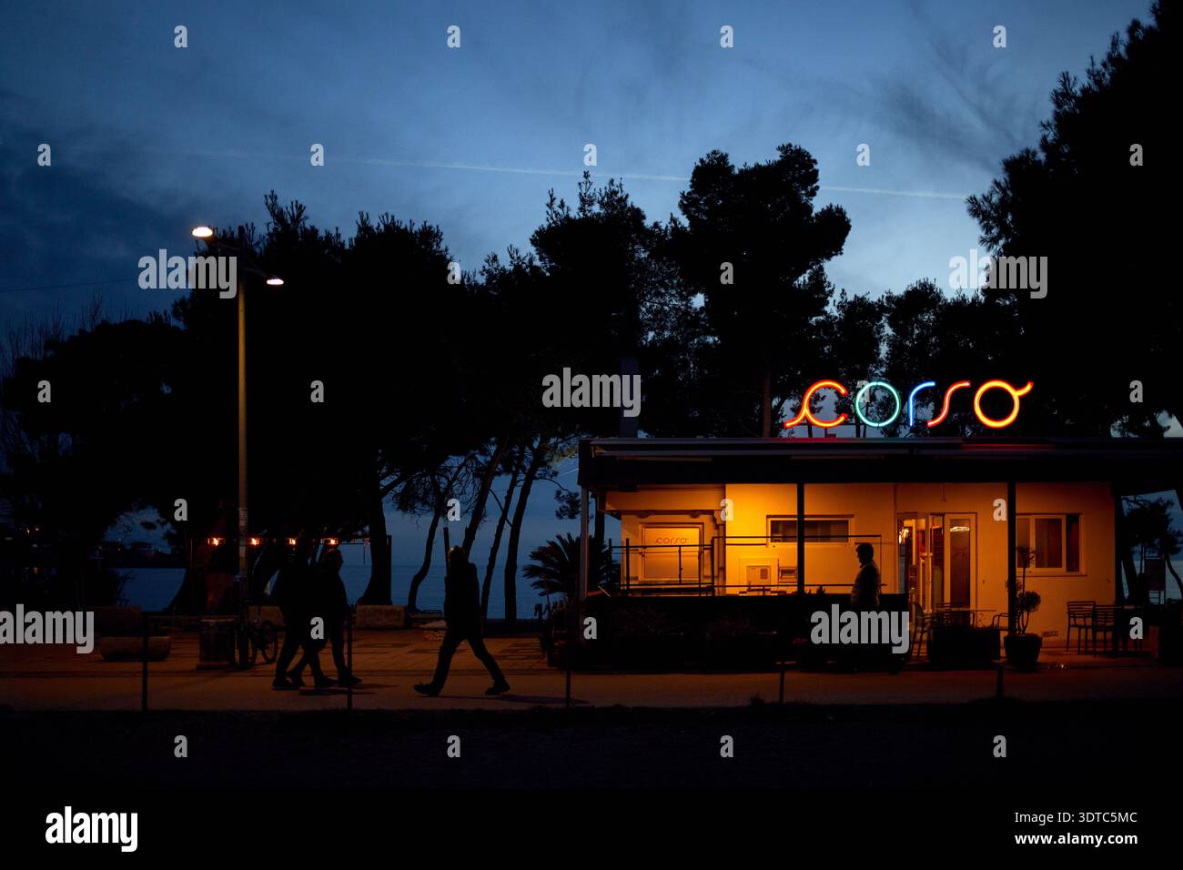 Bar, Monténégro – 08 février 2026 : café Corso illuminé au crépuscule avec des gens marchant le long de la promenade du bord de mer Banque D'Images