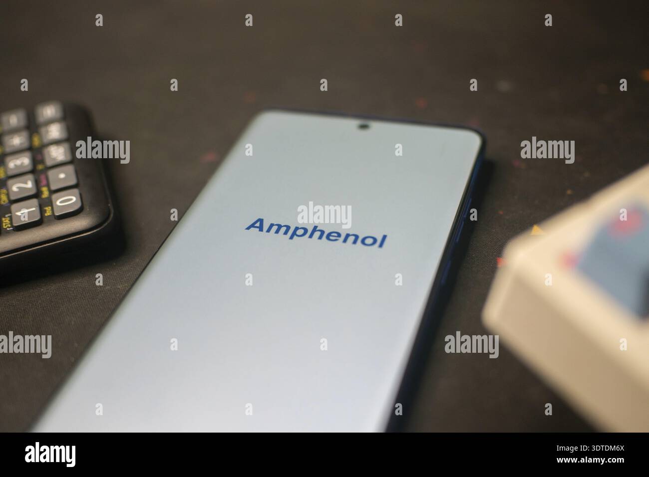 Téléphone affichant le logo Amphenol près d'une calculatrice sur un bureau Banque D'Images