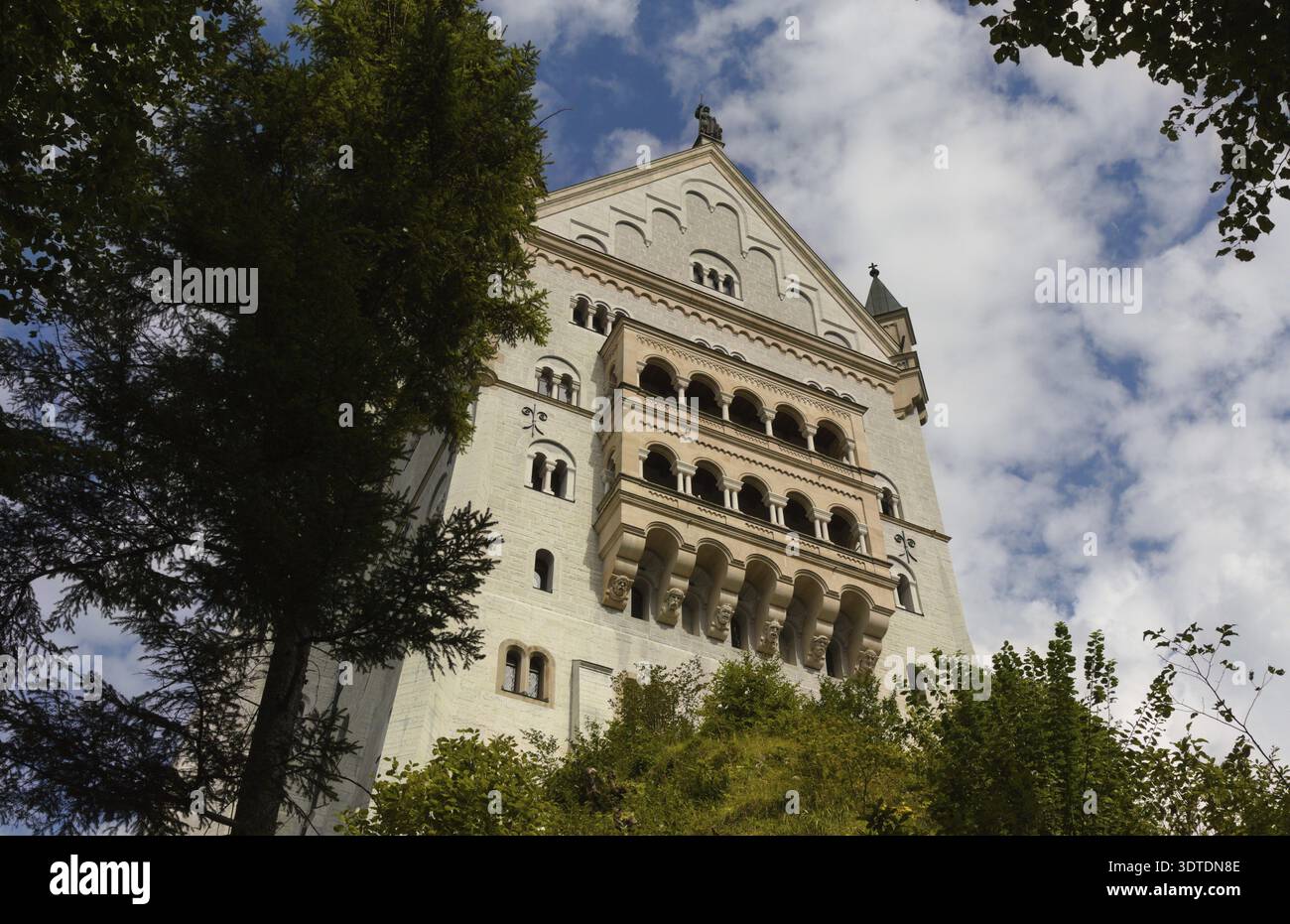 Château Neuschwanstein : une vue vers le haut d'une tour de château en pierre blanche avec des fenêtres cintrées entourées de grands arbres sous un ciel nuageux Banque D'Images