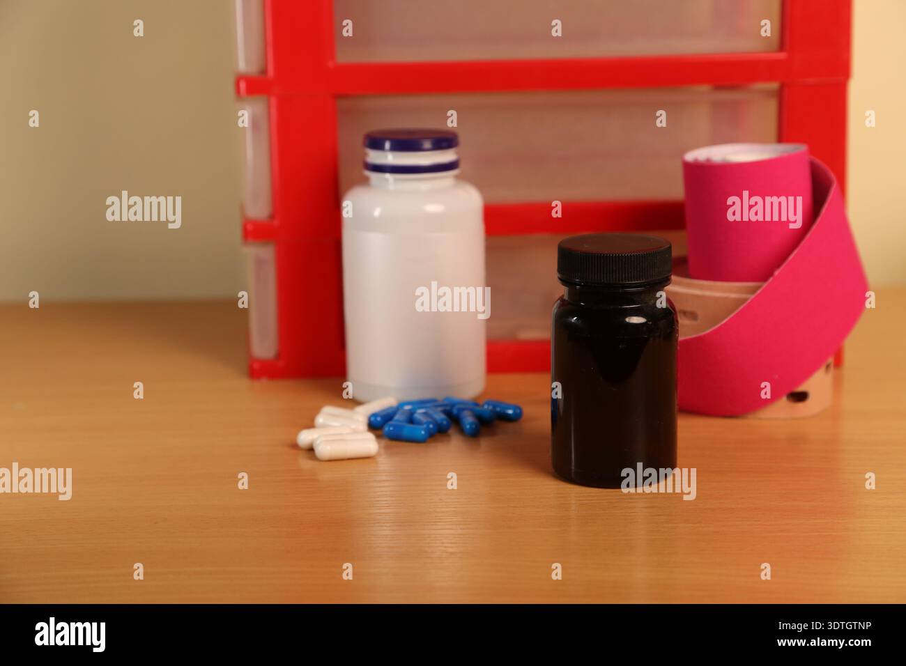 Une collection de médicaments est disposée sur une table. Il y a diverses bouteilles et pilules ainsi que des bandages. L'arrière-plan montre les conteneurs de stockage utilisés pour organiser les fournitures de santé. Photo de haute qualité Banque D'Images