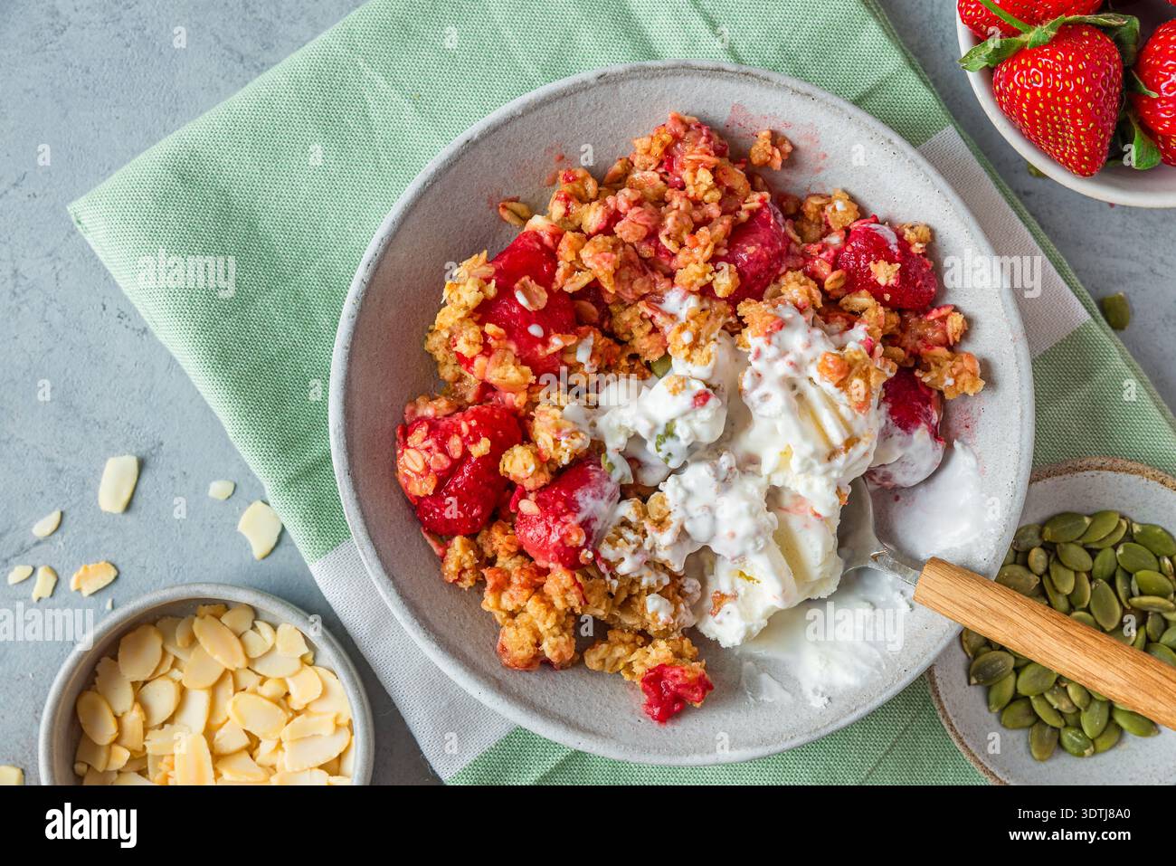 Crumble de fraise dessert avec crème glacée à la vanille fondante, granola cuit au four, graines de citrouille et amandes dans un bol avec cuillère sur fond gris. Fait maison Banque D'Images