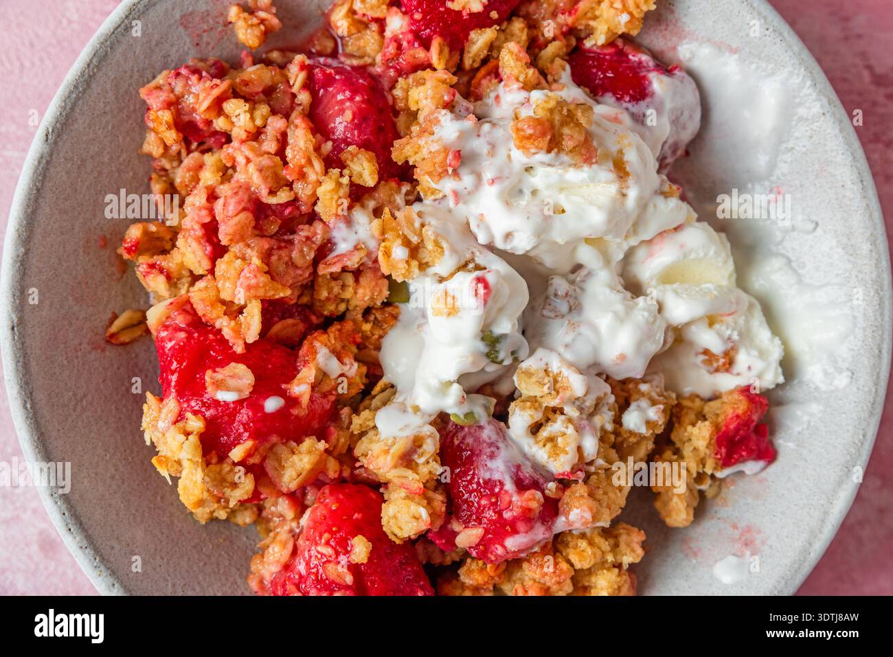 Crumble aux fraises avec crème glacée fondante, granola cuit au four, graines de citrouille et amandes dans un bol. Dessert aux fruits croustillants d'été. Pâtisserie sucrée maison avec Banque D'Images