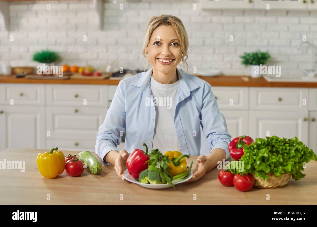 Portrait de jeune femme souriante heureuse assise à la table de cuisine avec des légumes frais Banque D'Images